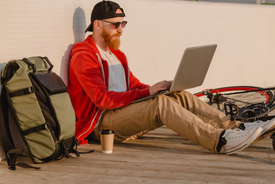 Digital nomad sitting outside with a laptop, backpack, and coffee, illustrating remote work in the digital nomad economy.