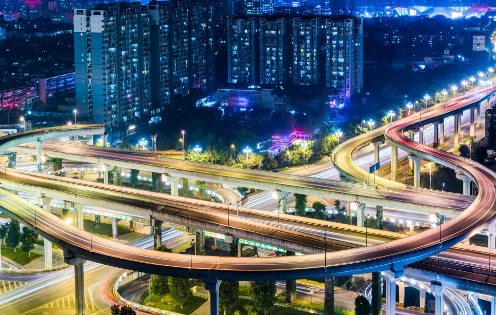 Aerial view of a lit multi-level highway interchange in a modern city at night, illustrating smart city transport.