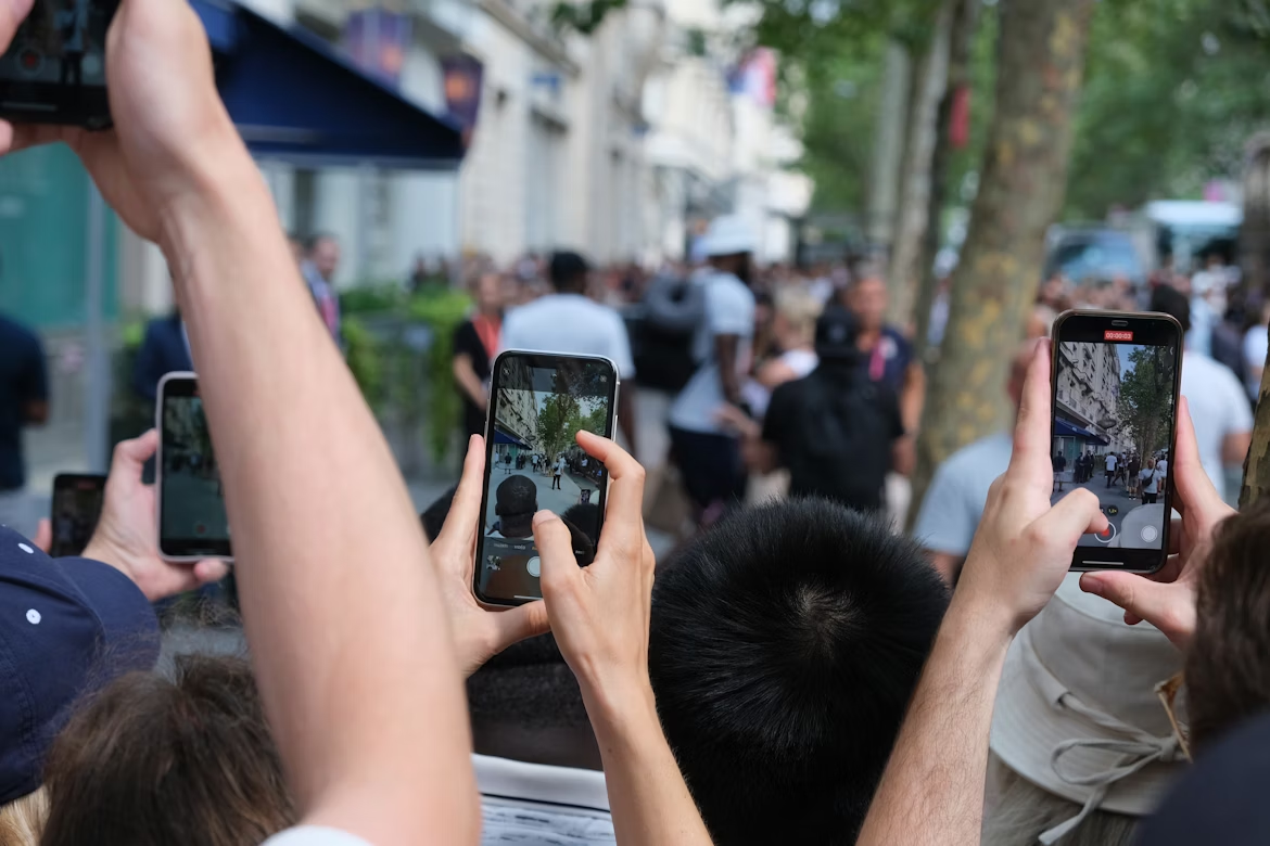 People in a crowd use smartphones to record a street protest, showing how social media captures social movements.