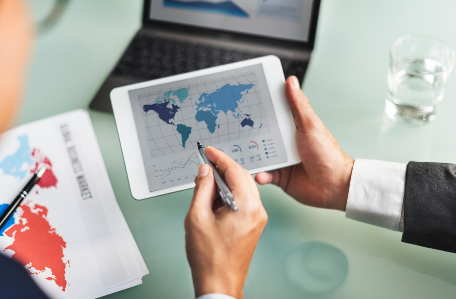 Professional reviewing a world map and trade statistics on a tablet, illustrating post-pandemic global trade routes.