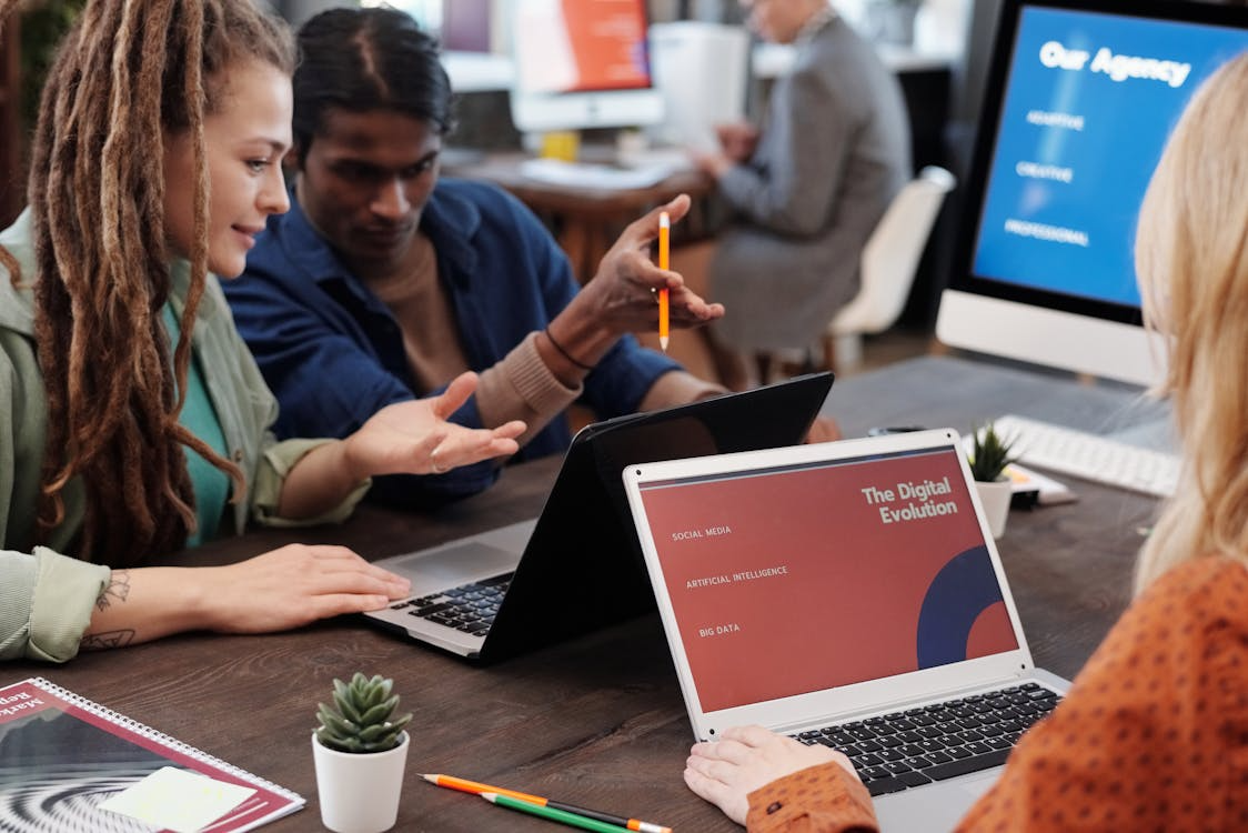 Coworkers collaborating on laptops in a modern office, discussing flexible work in a technology-driven workplace.