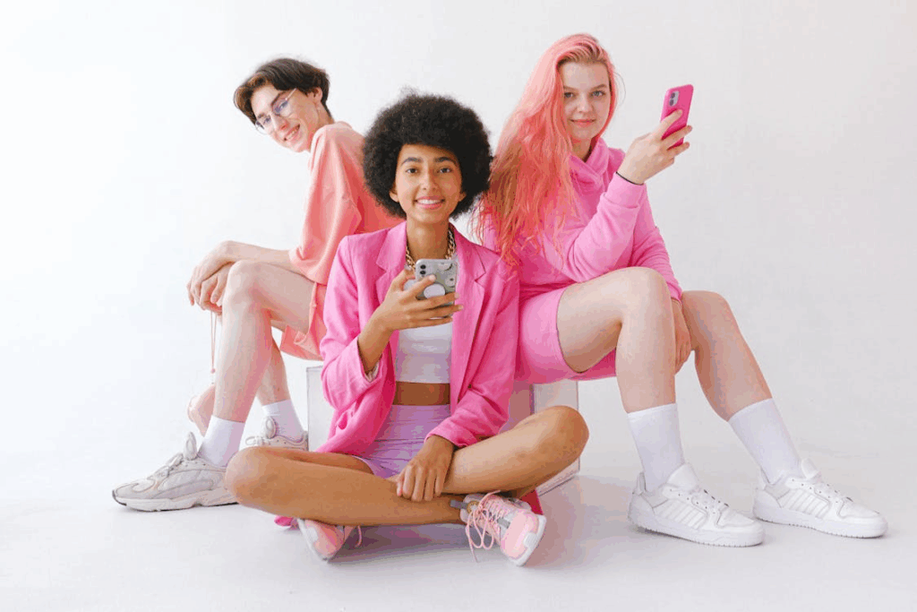 Three Gen Z friends in bright pink outfits with smartphones, representing modern digital-native consumers.