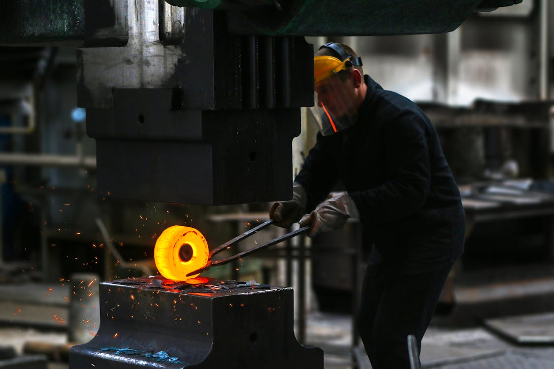Industrial steelworker using heavy machinery to forge metal, illustrating traditional processes shifting toward green steel manufacturing.