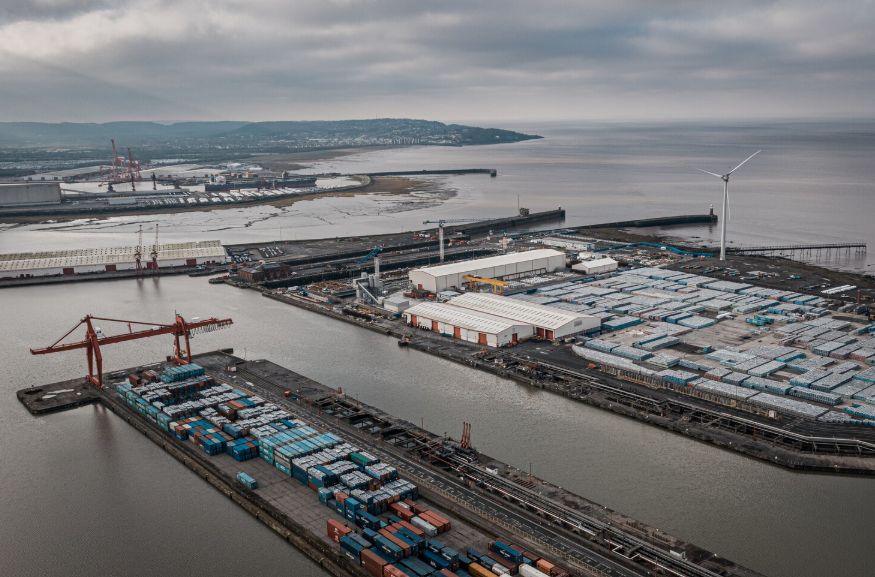 Aerial view of a coastal container port with warehouses and cargo stacks, highlighting how global supply chains rely on logistics hubs.